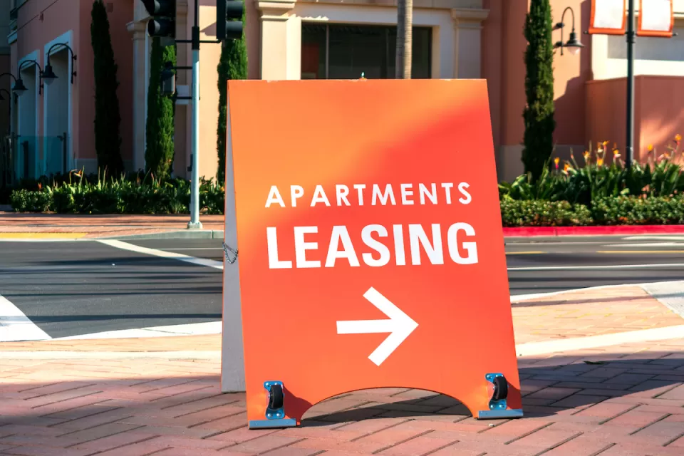 Orange "Apartments Leasing" sandwich board sign on sidewalk with arrow pointing right.